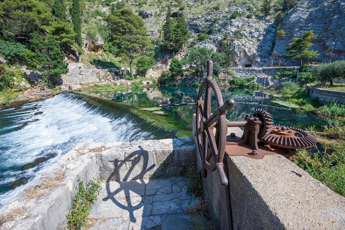Rusty iron mill wheel beside the weir at the Ombla river spring