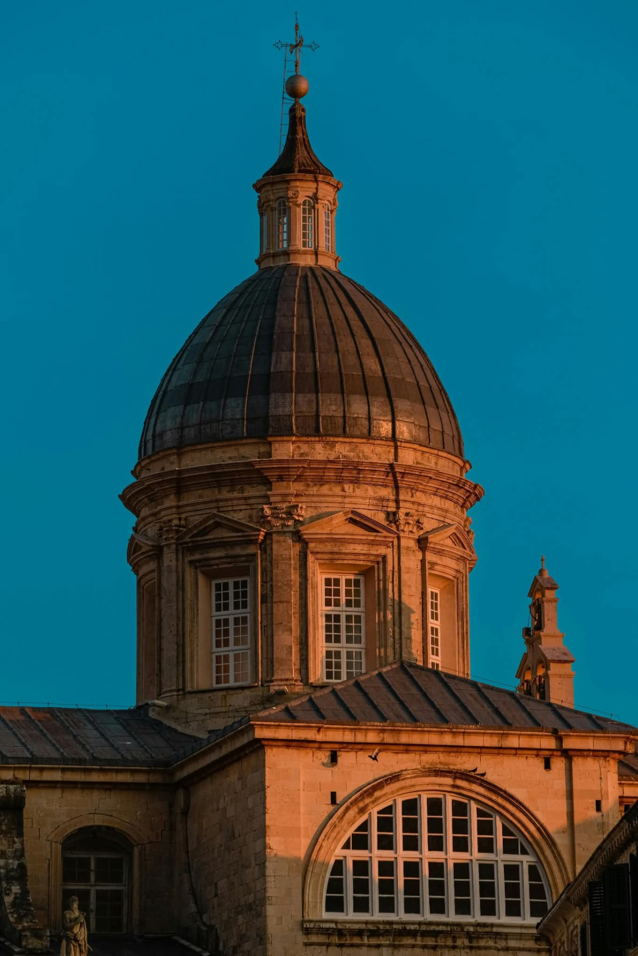 Dubrovnik Cathedral dome lit by golden evening light against a deep blue sky
